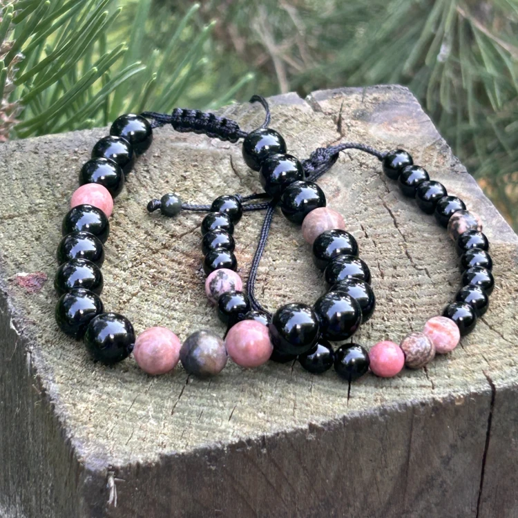 Zestaw dwóch bransoletek dla pary z rodonitu i obsydianu na czarnym sznurku leżący na surowym dębowym blacie w pracowni TEJE.